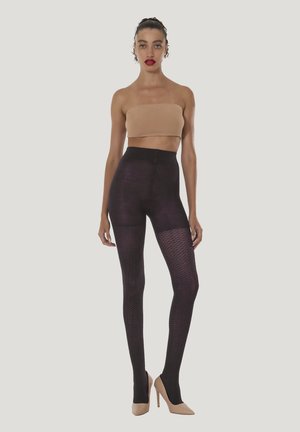 Højttaljede, strukturerede leggings i mørk lilla med netmønster. Modellen bærer en nøgen bandeau-top og beige højhælede sko.