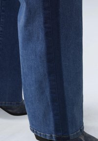 Wijd-uitlopende denim broek met een donkerblauwe zijstreep, een lichtblauwe wassing en zichtbare stikseldetails aan de zoom en zijnaden.