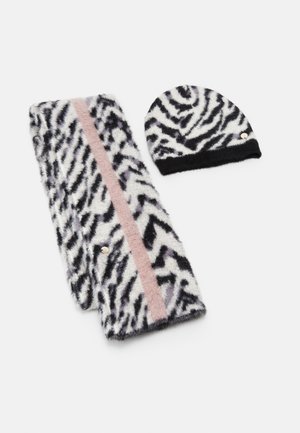 Écharpe en laine douce et bonnet avec imprimé zèbre noir et blanc, l'écharpe présentant une bande verticale rose et de petites étiquettes métalliques avec logo.