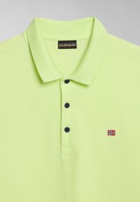 Limetkově zelená polo košile vyrobená z texturované tkaniny, obsahuje tříknoflíkovou légu, námořnické knoflíky a malou vyšívanou vlajkovou logo na hrudi.
