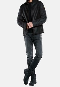 Mustahommasta nahasta valmistettu takki, jossa on pehmustetut hihat, etuvetoketju ja korkea kaulus. Yhdistetty tummanharmaisiin farkkuihin ja mustiin saappaisiin. Sileä pinta ja istuva muotoilu.