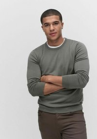 Grå crewneck-tröja med ribbade mudd och nederkant, tillsammans med bruna byxor. Tyget ser slätt och figursytt ut, vilket ger en avslappnad look.