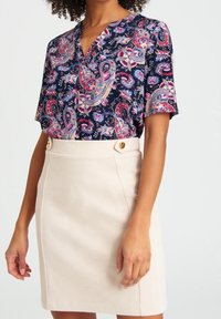 Marinblå blommig blus med korta ärmar och V-ringning, tillsammans med en beige pennkjol med två guldknappar vid midjan.