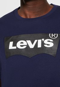 T-shirt en coton bleu marine avec un grand logo noir Levi's et des lettres blanches, centré sur la poitrine. Manches courtes, col rond.