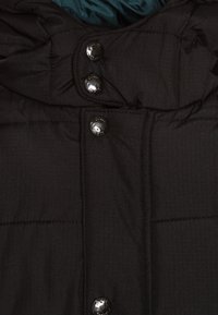 Giacca a vento nera con texture trapuntata, colletto alto e tre bottoni lucidi sul davanti, con una fodera interna in teal a contrasto.