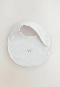 Vitt bomullsnappar med prickigt mönster och en ljusblå broderad sløyfa. Fästs med två tryckknappar på sidan. Rundad form.