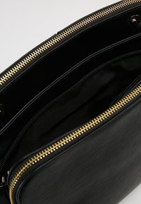 Czarna skórzana torba ze złotym zamkiem błyskawicznym, z gładką powierzchnią zewnętrzną i czarnym materiałowym wnętrzem. Zawiera wiele przegródek do organizacji.