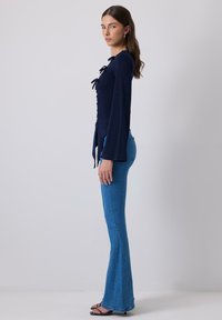 Navy blue long-sleeve top with lace-up front, paired with fitted blue flared jeans. The top has a textured finish and bell sleeves.
