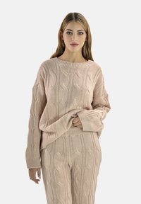 Helle rosa Strickjacke mit Zopfmuster, Rundhalsausschnitt und langen Ärmeln, kombiniert mit passenden strukturierten Hosen. Weicher Stoff.
