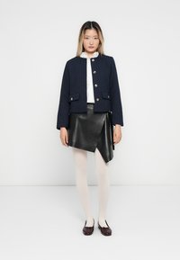 Námořnický prošívaný crop jacket se stříbrnými knoflíky, v kombinaci s černou koženou zavinovací sukní, nahými punčochami a vínovými baleríny.