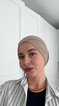 Beżowa chusta na głowę wykonana z miękkiego materiału, dobrze dopasowana, gładka w dotyku. Osoba nosi pasek w paski oraz pomarańczowy naszyjnik, z akcentami makijażu.