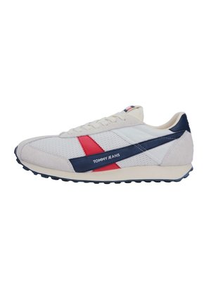 Zapatilla deportiva blanca Tommy Jeans con franjas diagonales en azul marino y rojo, parte superior de malla texturizada, suela beige y logo "TOMMY JEANS" en el costado.