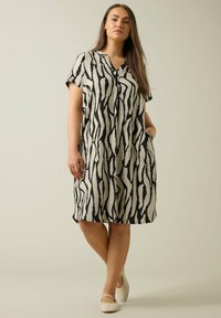 Kleid mit kurzen Ärmeln aus beigem Stoff mit einem schwarzen abstrakten Zebra-Muster, mit V-Ausschnitt und seitlichen Taschen für zusätzlichen Komfort.