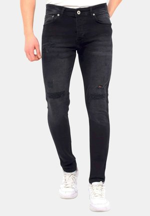 Zwarte denim skinny jeans met verwerkte details, inclusief scheuren bij de knieën en een middelhoge taille. Gepaarde met witte sneakers.