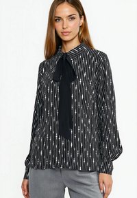 Czarna bluzka z pionowymi białymi paskami i kołnierzykiem z kokardą. Wykonana z lekkiego materiału o gładkiej fakturze i luźnym kroju.