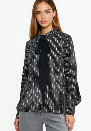 Czarna bluzka z pionowymi białymi paskami i kołnierzykiem z kokardą. Wykonana z lekkiego materiału o gładkiej fakturze i luźnym kroju.