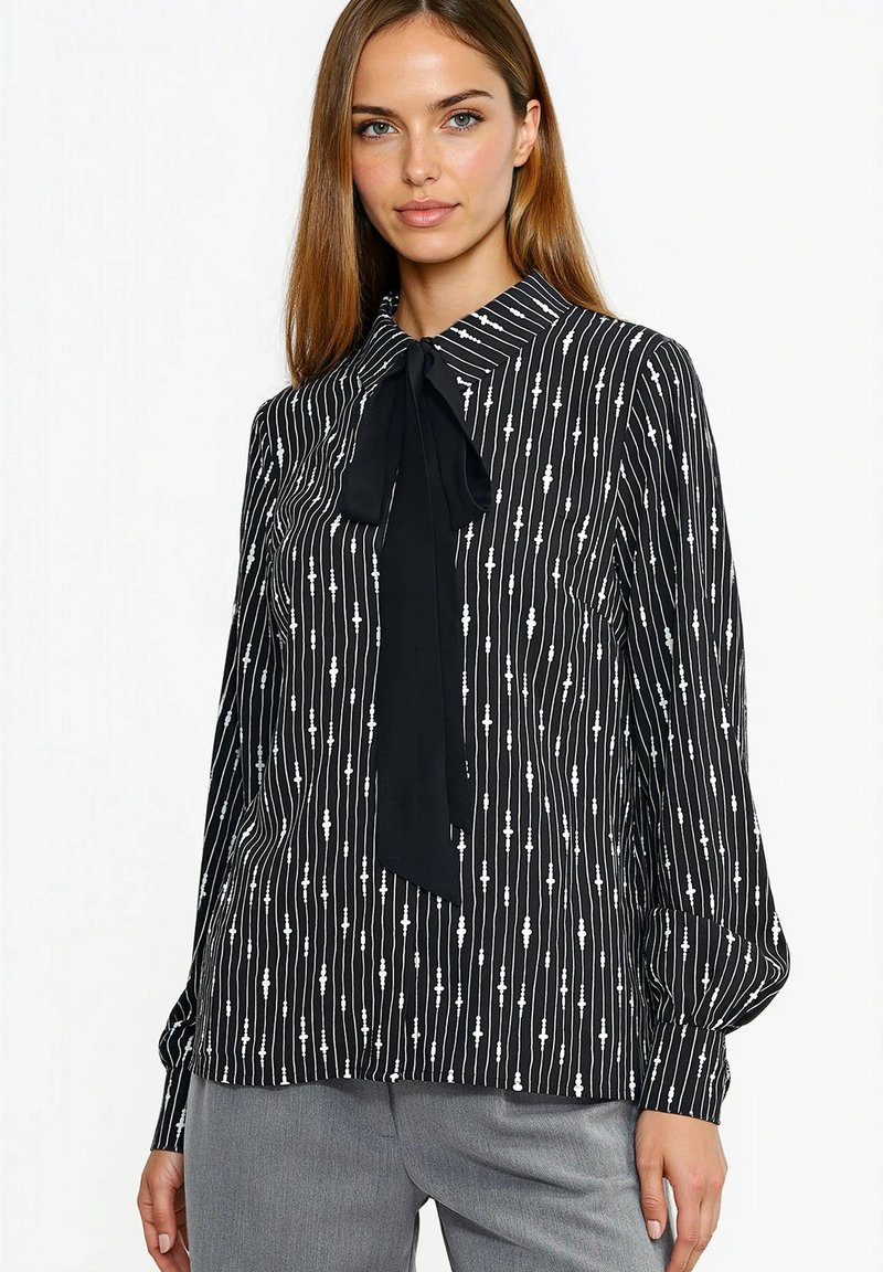 Czarna bluzka z pionowymi białymi paskami i kołnierzykiem z kokardą. Wykonana z lekkiego materiału o gładkiej fakturze i luźnym kroju.