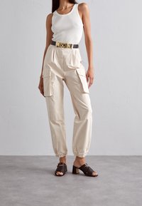 Beige cargobyxor med elastiska muddar, matchade med en vit ribbad tanktopp och bruna sandaler med klack och öppen tå. Guldig Moschino-bälte.