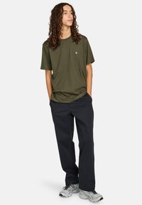 T-shirt vert olive à col rond, associé à un pantalon bleu marine et des baskets grises. La tenue a une coupe décontractée et un style informel.