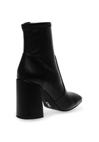 Mustat nahkasaappaat nilkkapituisella, paksulla korolla, terävä kärki ja elastiset sivut, joissa on hillitty metallinen yksityiskohta kannassa.