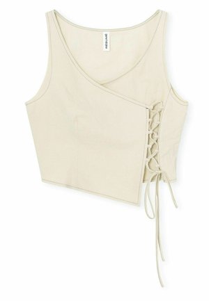 Light beige cropped tank top with a wrap design, featuring a lace-up side detail and smooth textured fabric. Label reads "RÉSUMÉ."