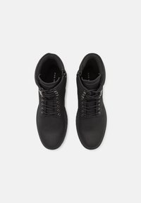 Botas negras de tobillo de cuero con una textura suave, que presentan un cierre con cordones y ojales en tono plateado, diseño minimalista.