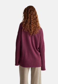 Lila übergroßer Pullover mit gerippten Akzenten an Ärmeln und Saum. Weicher, strukturierter Stoff fällt bequem über beigen Hosen.