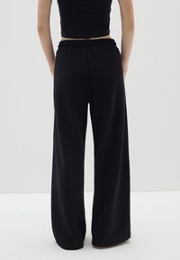 Pantalones de chándal anchos y negros, fabricados en un tejido suave, con una cinturilla elástica y un corte relajado. Sin patrones ni acentos visibles.