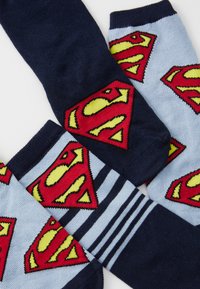 Superhjälte-tema strumpor i marinblå och ljusblå. Har gula och röda Superman-loggor, med randigt mönster på ett par. Tillverkat av bomull.