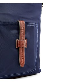 Borsa in tessuto blu navy con manico in pelle marrone dotato di fibbia, accentuata da cuciture bianche a contrasto. Texture liscia, design minimalista.