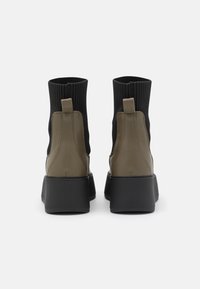 Black and olive green ankle boots with ribbed textile upper, smooth leather accents, and a chunky black sole; features a pull tab.
