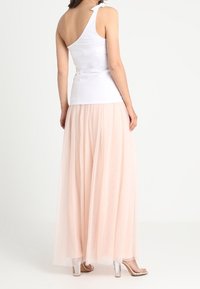 Een eenzijdige witte top gecombineerd met een lange, zachte, roze tule rok. Doorzichtige hak sandalen complementeren de outfit. Gladde stoftextuur.