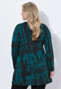 Langarm tuniek in teal en zwart met abstracte patronen. Kenmerkt zich door een relaxed fit, ronde halslijn en een zoom die op heuphoogte eindigt. Zachte stof textuur.