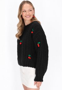 Čierny pletený sveter s 3D výšivkou čerešní v červenej a zelenej farbe. Hralý povrch s voľným strihom a spadnutými ramenami.