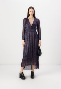 Violet, klostuoti midi suknelė su ilgomis rankovėmis ir giliu V formos iškirpimu. Su tekstūruotu audiniu ir prigludusia juosme. Juoda aksesuarų rankinė.