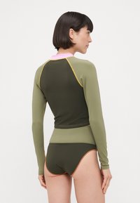 Rash guard a maniche lunghe, verde oliva con colletto rosa e accenti arancioni, abbinato a slip bikini coordinati. Tessuto morbido e elastico.
