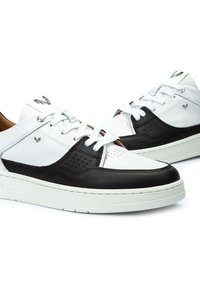 Zapatillas que presentan una combinación de cuero blanco y negro, acentos perforados, cordones blancos y una suela de goma texturizada con un diseño limpio.