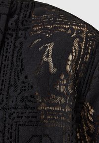 Tela de encaje negro con patrones y texturas intrincadas, con una mezcla de secciones opacas y transparentes, creando un efecto visual en capas.