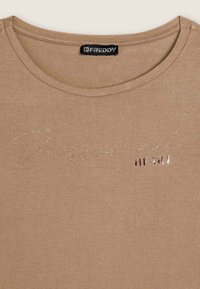 T-shirt marrone con scollatura rotonda e maniche corte. Presenta la scritta silver "Inspire" e "HEART" in rilievo con dettaglio metallico.