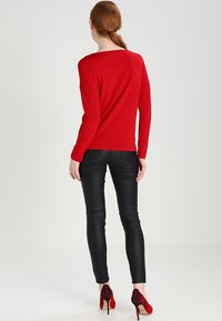 Rode blouse met lange mouwen, zwarte strakke broek en bordeauxrode hoge hakken. Glad textuur, eenvoudig ontwerp, getoond vanuit de achterkant.