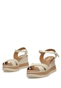 Sandalias de plataforma beige con un acabado de cuero brillante, que presentan tiras cruzadas, una correa de tobillo ajustable y una suela texturizada para mayor agarre.