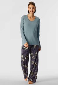 Top azzurro chiaro a maniche lunghe con scollatura a V, abbinato a pantaloni da pigiama a gamba larga con un motivo floreale su uno sfondo viola scuro.