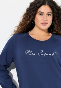 Felpa blu navy con scollatura rotonda, caratterizzata da un testo ricamato bianco "New Casual" sul davanti e maniche lunghe. Tessuto morbido.