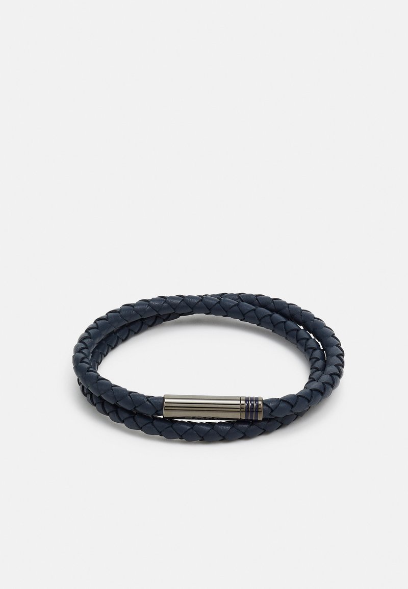 Il bracciale in pelle intrecciata di colore blu navy presenta una chiusura metallica elegante con scanalature sottili, che mette in mostra una texture dettagliata e una forma circolare.