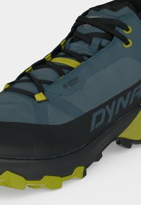 Μπλε και μαύρο ορειβατικό παπούτσι με κίτρινες λεπτομέρειες, μαύρα κορδόνια, σήμανση GORE-TEX και ανθεκτική σόλα σχεδιασμένη για υπαίθρια χρήση.