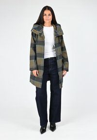 Manteau à carreaux imperméable en vert olive et marine, doté d'une capuche, d'une fermeture éclair, de manches longues et de poches latérales, associé à un pantalon en denim foncé.