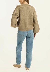 Beiger gerippter Strickpullover mit Rundhalsausschnitt und voluminösen Ärmeln, kombiniert mit hellblauen geraden Jeans und beigen Slippers.