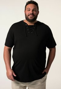 Černé tričko s krátkým rukávem a šněrovacím výstřihem, vyrobené z jemné látky. Disponuje volným střihem a hladkým povrchem.