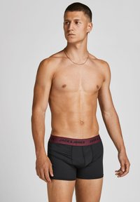 Schwarze Boxer Shorts mit einem bordeauxfarbenen Gummibund, der "JACK & JONES" in schwarzer Schrift zeigt. Glattes Material mit einem enganliegenden Design.
