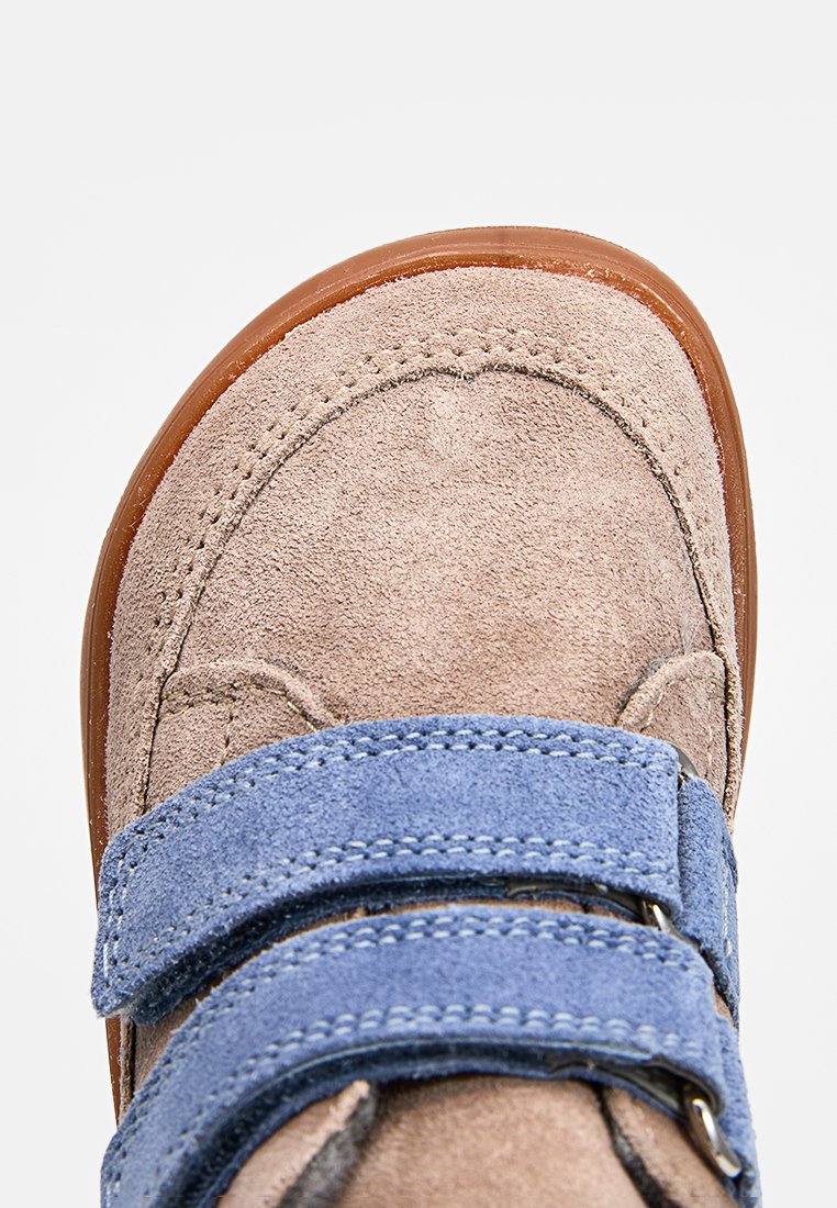 Zapato de ante marrón claro con punta redonda, que cuenta con dos correas de Velcro azul. Suela de goma y detalles cosidos a lo largo de los bordes.